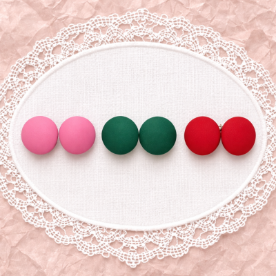 Botões coloridos em tecido, dispostos em pares sobre fundo branco com renda, sobre papel rosa amassado.