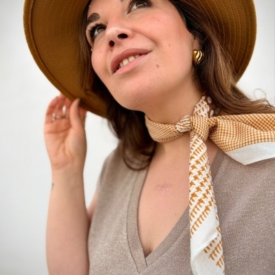Mulher com chapéu castanho, lenço estampado e brincos dourados