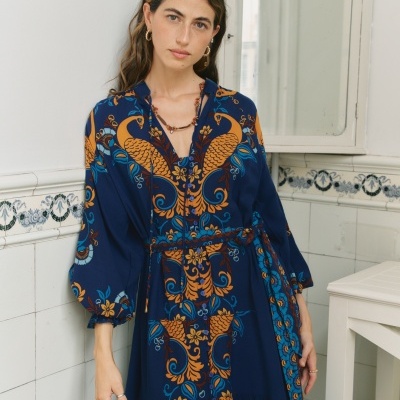 Vestido comprido azul escuro com padrão de pavões alaranjados e detalhes florais.