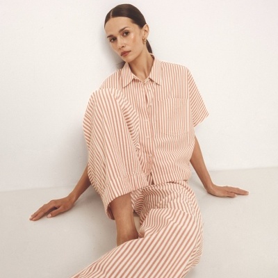 Pijama às riscas branco e castanho claro com camisa de botões e calças largas em fundo branco