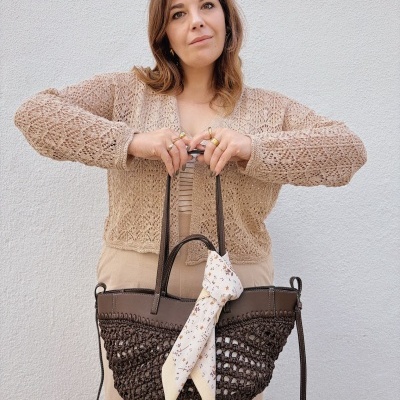 Mulher com cardigan bege segurando mala castanha com lenço bege amarrado