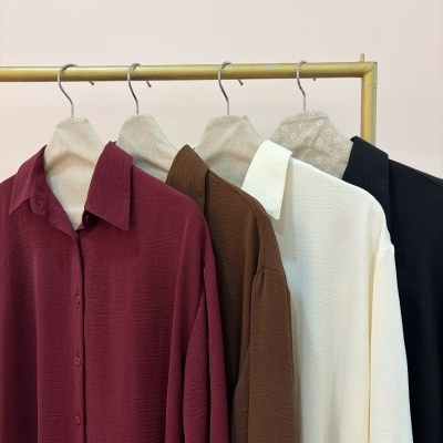 Quatro camisas em diferentes cores penduradas num suporte metálico dourado
