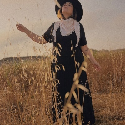 Mulher de vestido preto, chapéu e lenço branco em campo seco