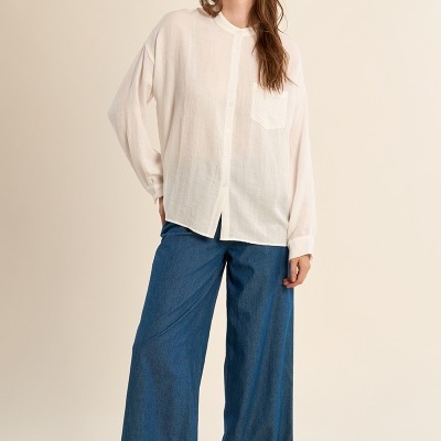 Mulher com camisa branca e calças largas de ganga azul em fundo neutro