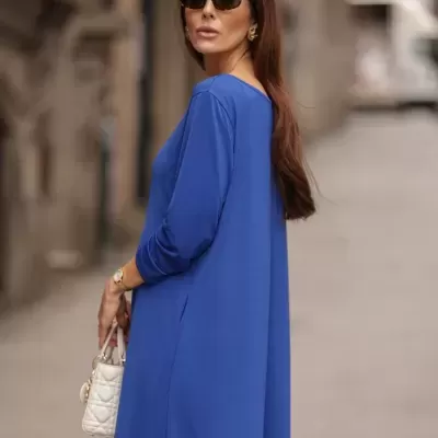 Mulher com vestido azul e mala branca num cenário urbano.