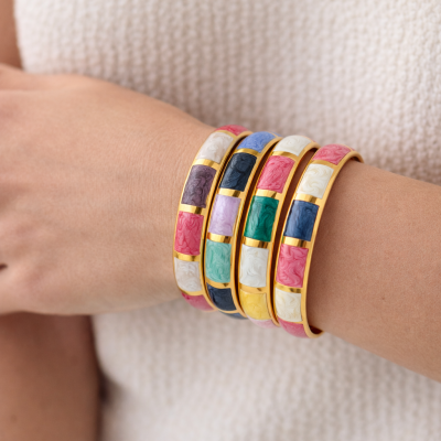 Pulseiras coloridas em base dourada com padrão marmoreado no pulso de uma pessoa.