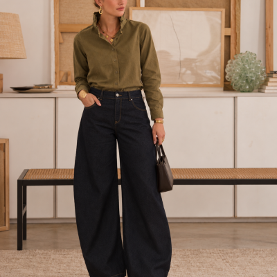 Mulher com camisa verde-oliva e calças largas de ganga azul escura em ambiente interior