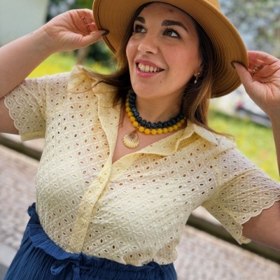 Mulher com chapéu castanho claro, camisa amarela bordada, saia azul escura e colar colorido.