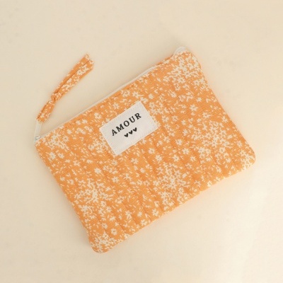 Necessaire laranja com padrão floral branco e etiqueta AMOUR.