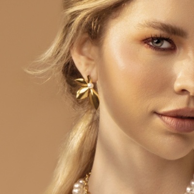 Mulher com brincos dourados e colar de pérolas em fundo bege