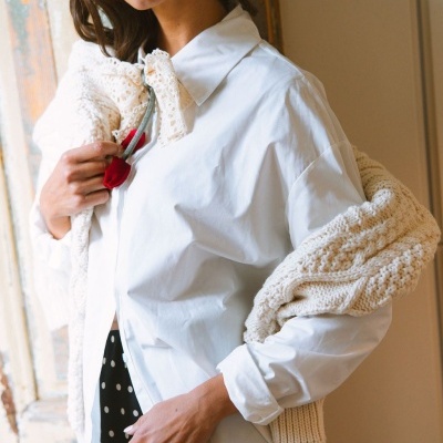 Mulher com camisa branca, vestido preto de bolinhas e suéter de malha creme