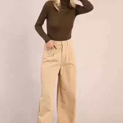 Mulher com camisola castanha e calças largas bege em fundo neutro