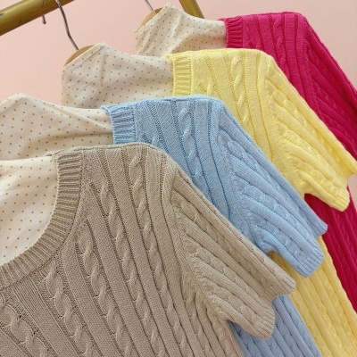 Camisolas de malha coloridas com padrão de trança penduradas em cabides com camisa branca de bolinhas