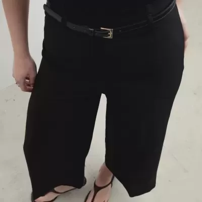 Pessoas a usar calças largas pretas com cinto preto de fivela dourada e sandálias negras.