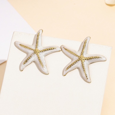 Brincos estrela do mar em branco e dourado sobre suporte branco.