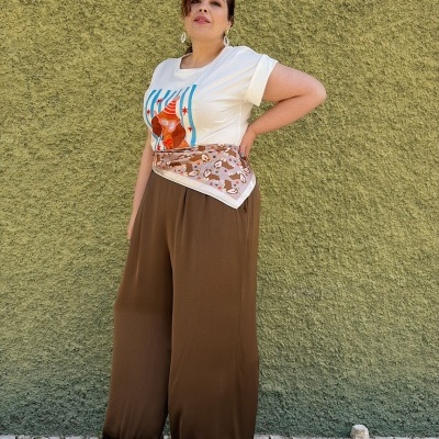 Mulher com t-shirt estampada e calças largas castanhas junto a parede verde