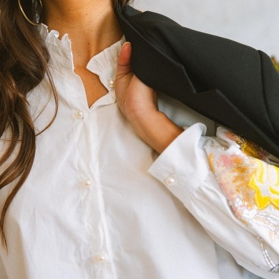 Blusa branca com botões de pérola e punhos bordados, combinada com blazer preto ao ombro