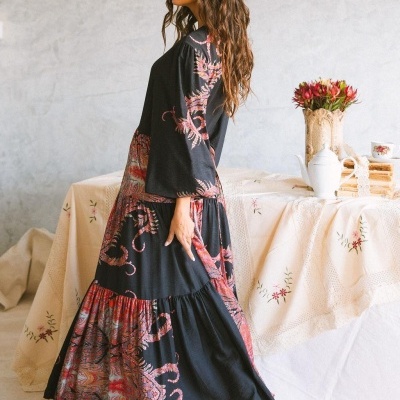 Vestido longo preto com padrões vermelhos e rosados usado por mulher de perfil