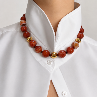 Colar com contas grandes castanho-avermelhado e douradas, camisa branca de gola alta