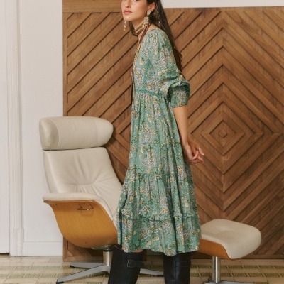 Vestido comprido verde com padrão floral, usado com botas pretas e cadeira de couro ao fundo