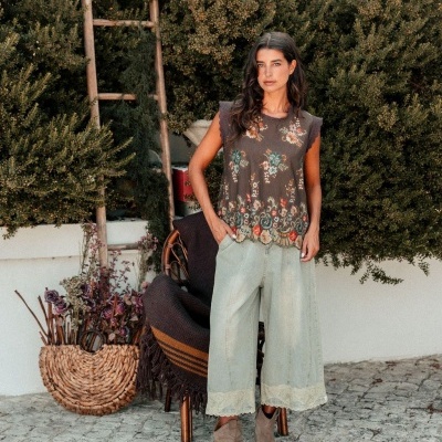 Mulher com blusa floral e calças largas azul claro em ambiente externo com plantas