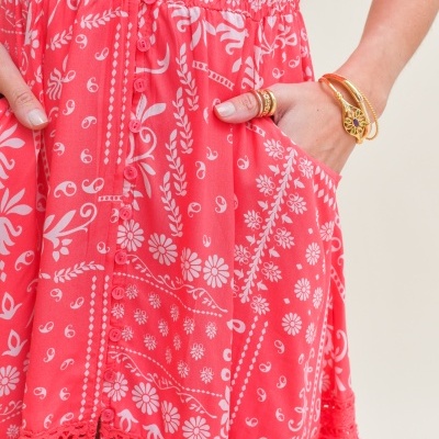 Vestido coral com padrão floral branco e detalhes em renda, mão com joias douradas