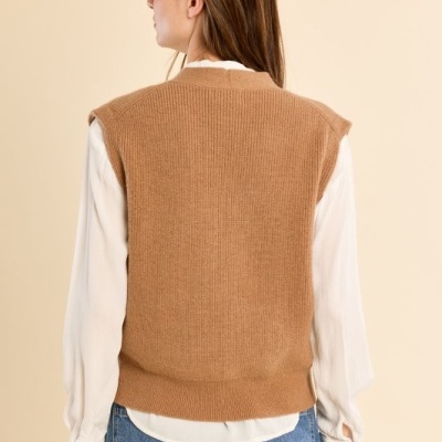 Mulher vista de costas com colete castanho, camisa branca e jeans azuis