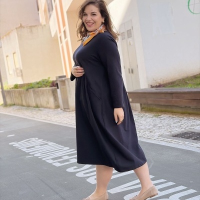 Mulher com vestido comprido preto e lenço amarelo ao pescoço em rua urbana