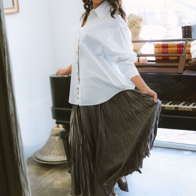 Mulher com camisa branca e saia plissada cinza escuro em ambiente com piano e decoração clássica