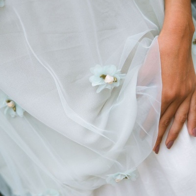 Detalhe de tecido branco com tule e flores azuis claras decorativas e mão morena