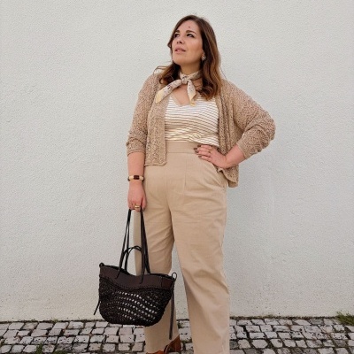 Mulher vestida com casaco bege, calças bege, sandálias castanhas e mochila preta trançada