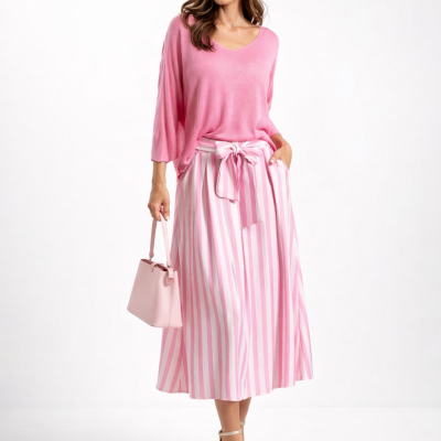 Mulher com camisola rosa, saia às riscas roxa e branca, sandálias bege e mala rosa claro.