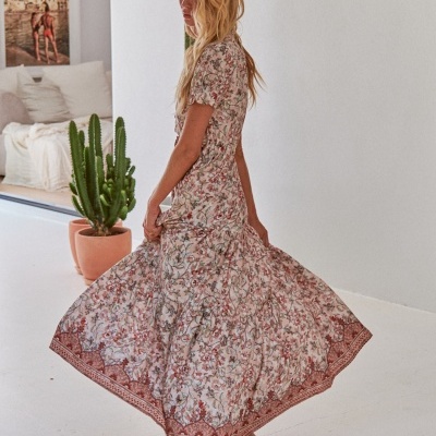 Vestido longo floral em tons de rosa e castanho com cós ajustado, usado por mulher loira em ambiente branco com cactos.