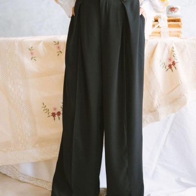 Calças pretas largas com cintura subida, bolsos laterais, usadas com camisa branca e sapatos castanhos