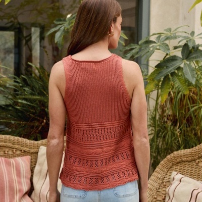 Top tricotado cor de ferrugem com padrões variados, usado com calças de ganga num ambiente com plantas e cadeiras de vime