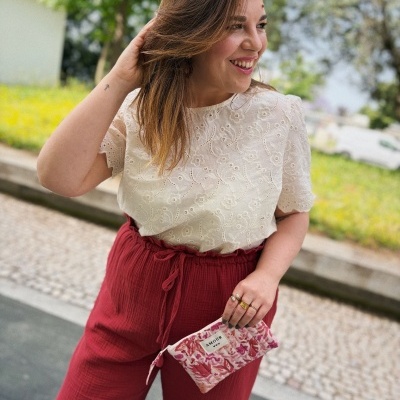Mulher com calças vermelhas de tecido leve, camiseta branca bordada e bolsa estampada rosa AMOUR ao ar livre