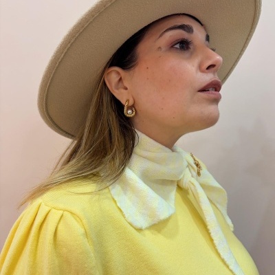 Mulher com chapéu bege de feltro e blusa amarela com lenço xadrez ao pescoço