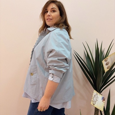 Mulher com camisa e casaco azul claro perto de planta decorativa com etiquetas.