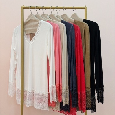 Sete blusas de manga comprida com renda na bainha e mangas em várias cores penduradas numa estrutura metálica.