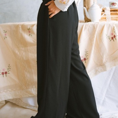 Calças pretas largas e fluídas com camisa branca bordada em ambiente com toalha e jarra branca.