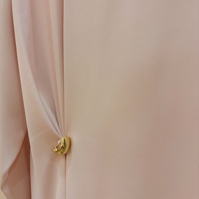 Tecido rosa claro preso por broche dourado