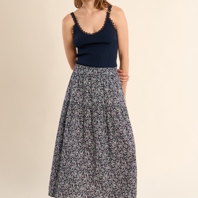 Mulher com top azul escuro de alças, saia longa floral e sandálias castanhas.