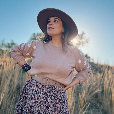 Mulher com chapéu castanho e camisola rosa com flores brancas ao ar livre