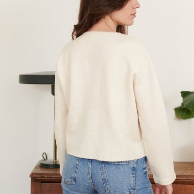 Mulher de costas com camisola bege e calças de ganga azuis em ambiente interior