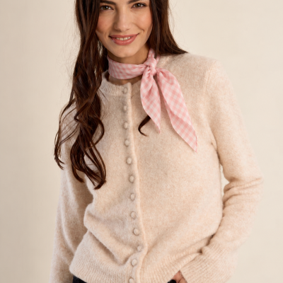 Mulher vestindo cardigan bege de malha com botões e lenço rosa xadrez no pescoço