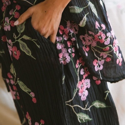 Detalhe de vestido preto com bordado floral rosa e verde e mão em bolso