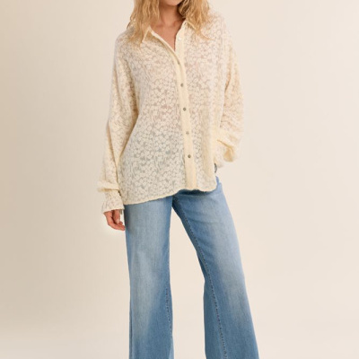 Mulher com cardigan de malha creme, jeans azuis largos e sapatilhas brancas em fundo neutro