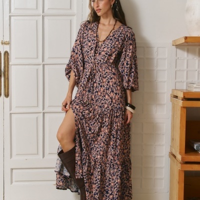 Mulher a usar vestido comprido floral azul e bege com mangas largas e botas castanhas em interior minimalista