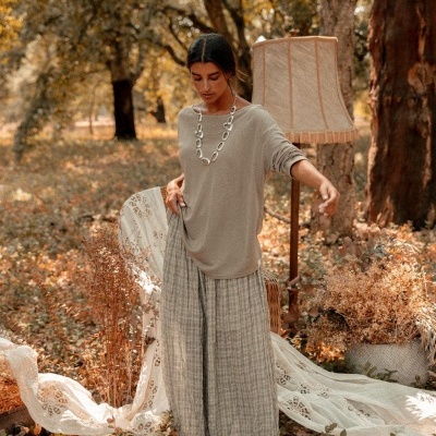 Mulher com camisola bege, pantalonas riscadas e colar prateado num cenário exterior outonal