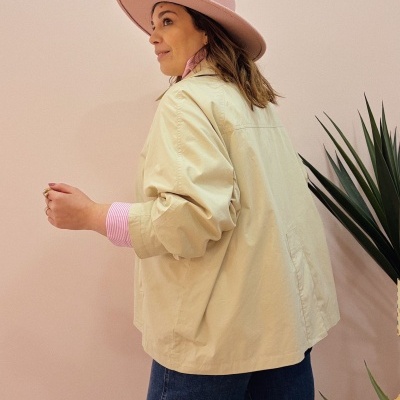 Mulher de perfil com casaco bege, camisa riscada rosa, chapéu rosa e jeans azuis